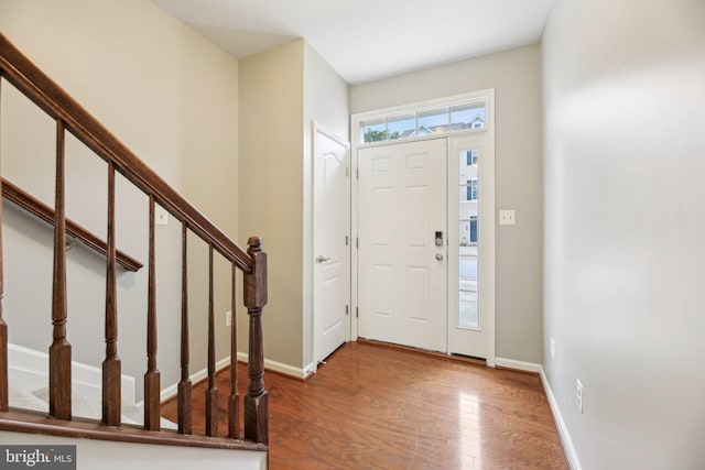 foyer entrance featuring wood finished floors, stairway, and baseboards