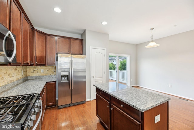 kitchen with appliances with stainless steel finishes, light wood-style floors, tasteful backsplash, a center island, and decorative light fixtures