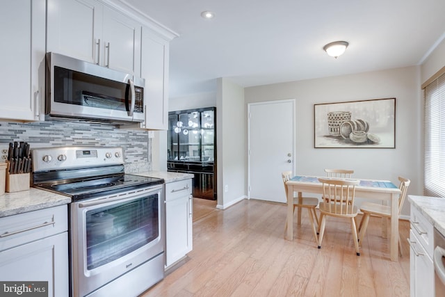 kitchen featuring stainless steel appliances, backsplash, light wood-style floors, white cabinetry, and light stone counters
