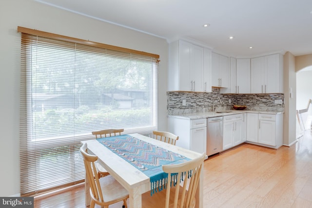 kitchen with stainless steel dishwasher, arched walkways, backsplash, a sink, and light wood-type flooring