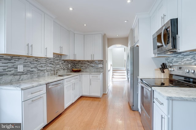 kitchen with appliances with stainless steel finishes, arched walkways, light wood-style floors, white cabinets, and recessed lighting