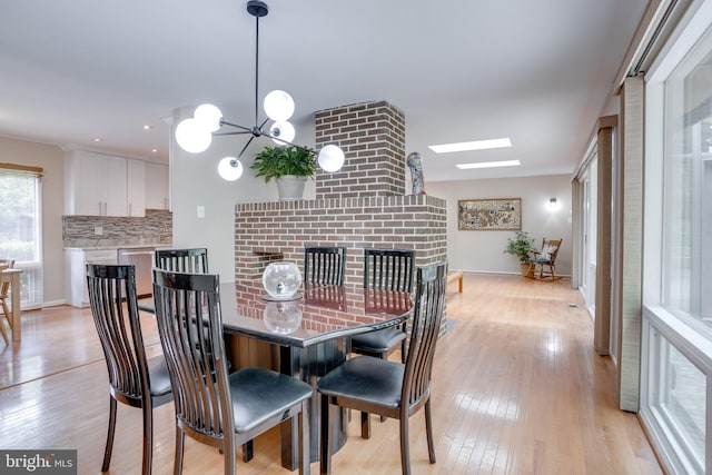 dining room featuring light wood-type flooring, a chandelier, baseboards, and a fireplace