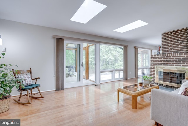 living area featuring a skylight, wood finished floors, a brick fireplace, and baseboards