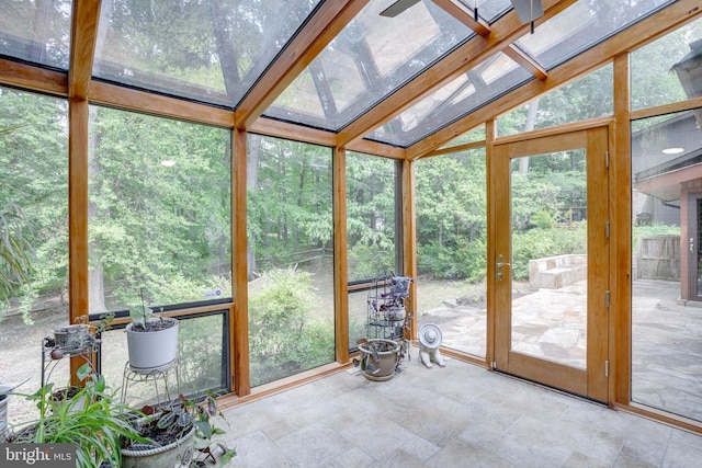 unfurnished sunroom with stone finish floors, a skylight, and lofted ceiling