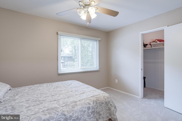 bedroom with a walk in closet, light carpet, a closet, baseboards, and ceiling fan