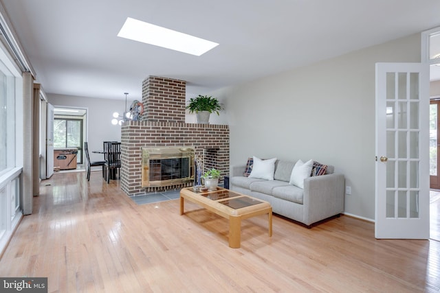 living area with light wood finished floors, a skylight, a fireplace, and a chandelier