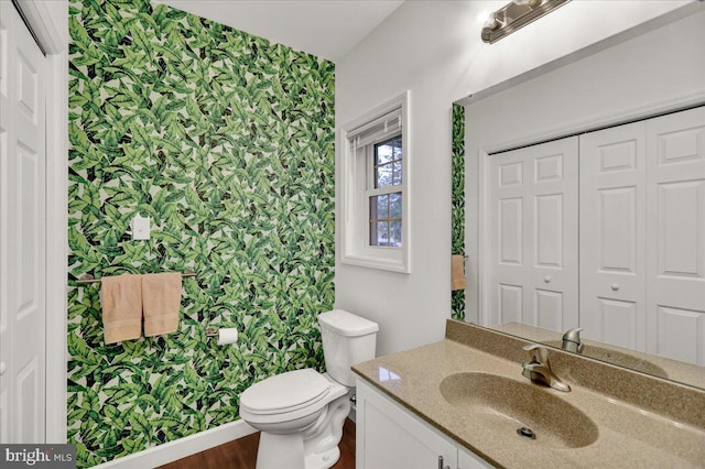 bathroom featuring wallpapered walls, an accent wall, toilet, vanity, and wood finished floors