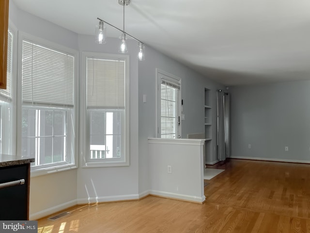 interior space featuring visible vents, baseboards, a healthy amount of sunlight, and wood finished floors