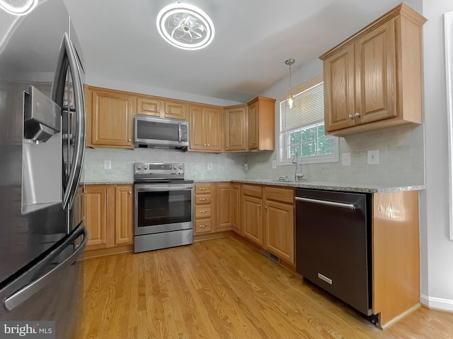 kitchen with a sink, light stone counters, light wood finished floors, decorative backsplash, and appliances with stainless steel finishes