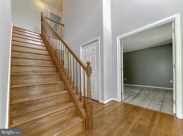 staircase featuring wood finished floors, baseboards, and a high ceiling