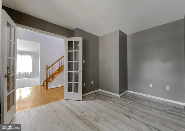 unfurnished room with wood finished floors, stairway, french doors, and baseboards