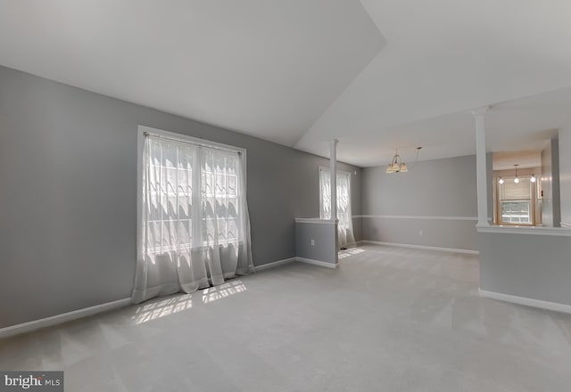 carpeted empty room featuring vaulted ceiling, baseboards, and decorative columns