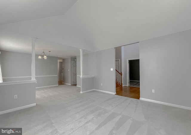 carpeted empty room with vaulted ceiling, baseboards, decorative columns, and stairs