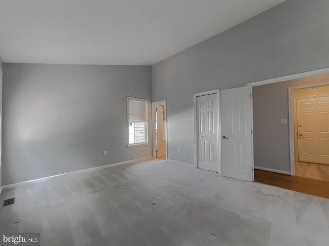 unfurnished bedroom featuring carpet, baseboards, and high vaulted ceiling