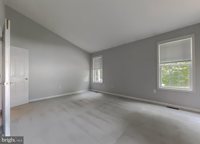 carpeted spare room featuring lofted ceiling, baseboards, and visible vents