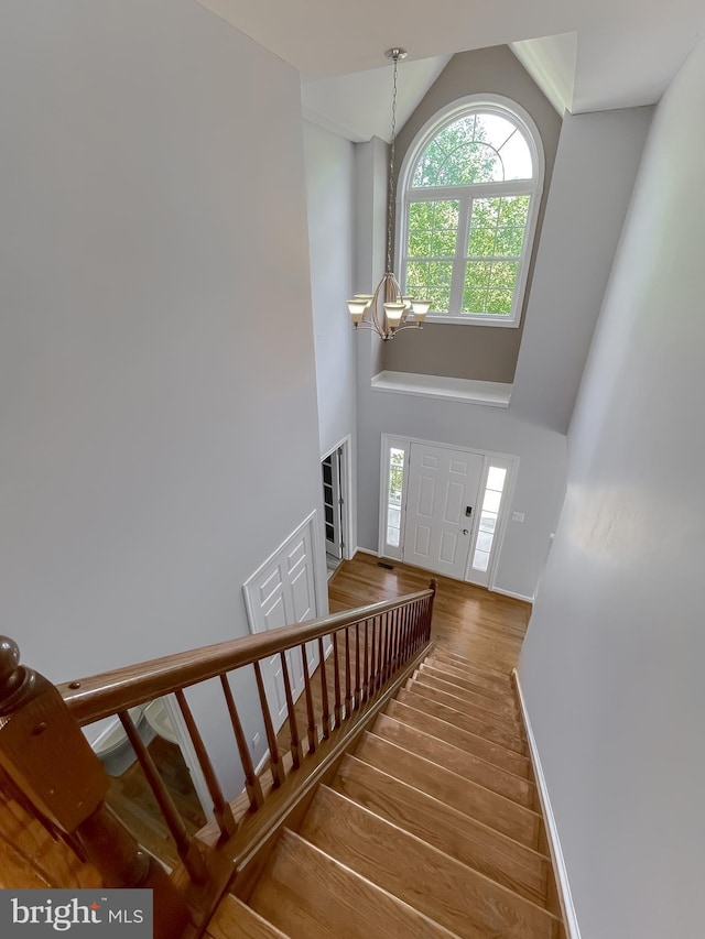 stairs with a wealth of natural light, a chandelier, high vaulted ceiling, and wood finished floors