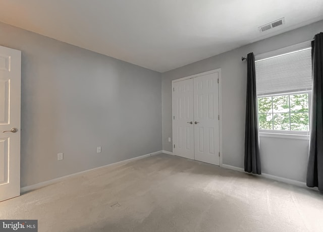 unfurnished bedroom with baseboards, a closet, visible vents, and light colored carpet