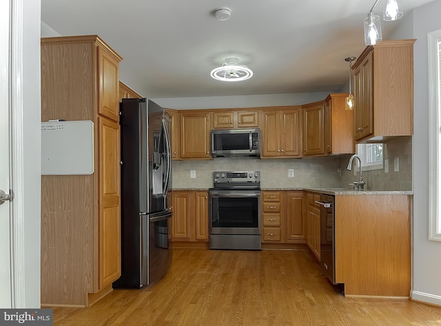 kitchen with light stone counters, stainless steel appliances, backsplash, and light wood-style flooring