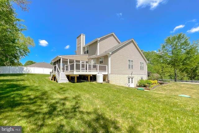 rear view of property featuring fence, a deck, a yard, a chimney, and a sunroom