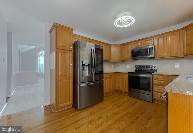 kitchen with light stone countertops, stainless steel appliances, tasteful backsplash, and light wood-style flooring