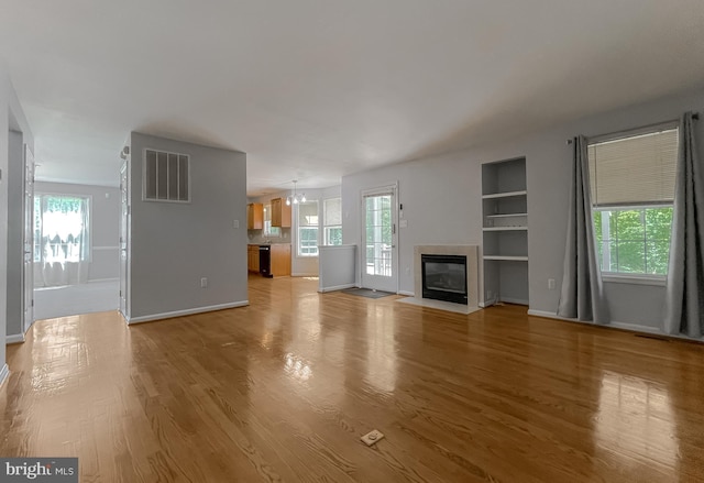 unfurnished living room with visible vents, built in shelves, baseboards, a fireplace with flush hearth, and light wood-style floors