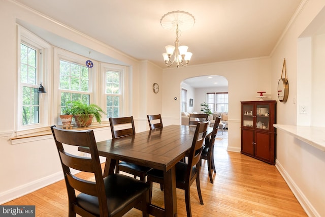 dining room with arched walkways, light wood finished floors, healthy amount of natural light, a chandelier, and crown molding
