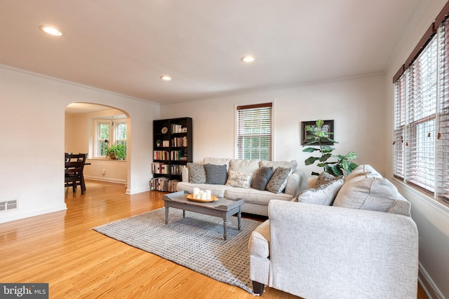 living room featuring arched walkways, crown molding, wood finished floors, recessed lighting, and baseboards
