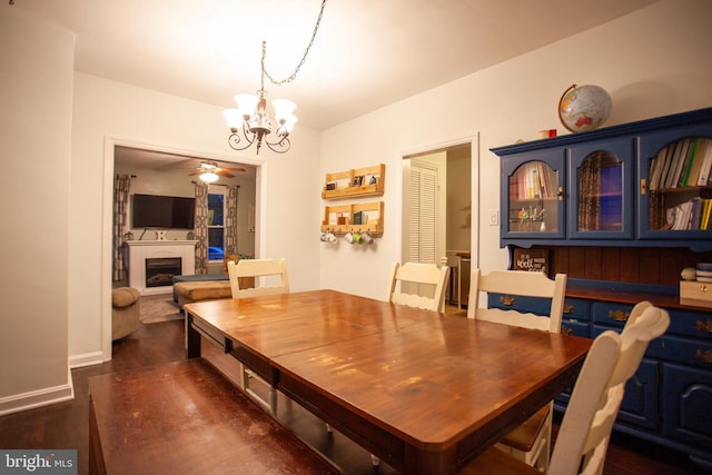 dining area with baseboards, a fireplace, ceiling fan with notable chandelier, and dark wood-style floors
