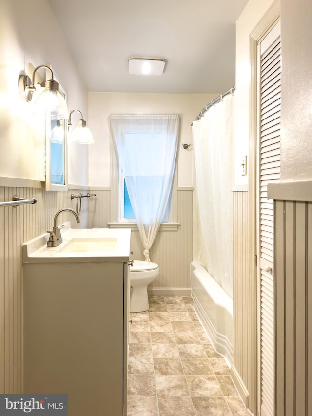 bathroom featuring toilet, vanity, shower / bath combination with curtain, and a wainscoted wall
