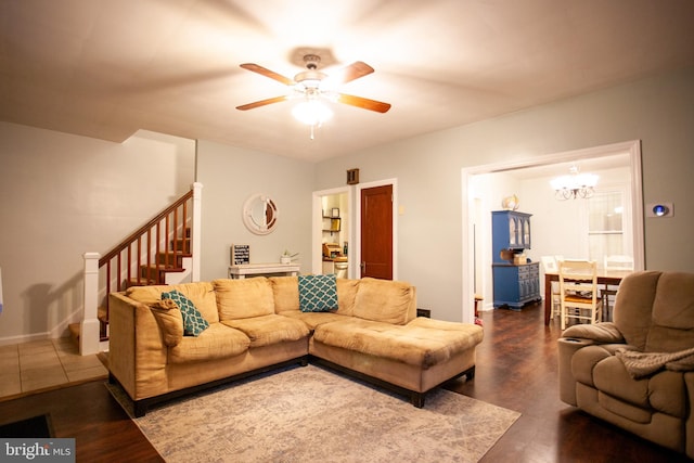 living room with baseboards, dark wood-style flooring, ceiling fan with notable chandelier, and stairs