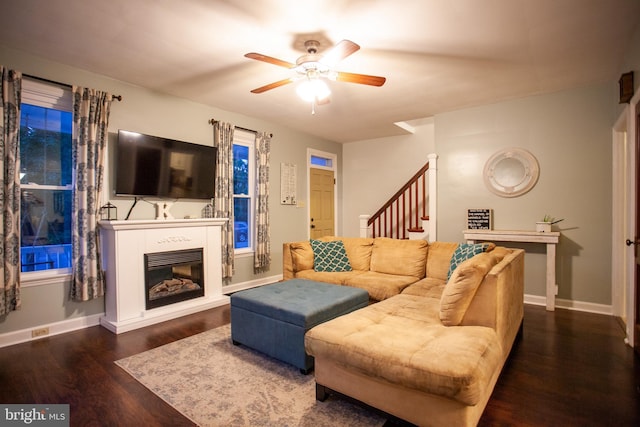 living room with stairs, wood finished floors, ceiling fan, baseboards, and a glass covered fireplace