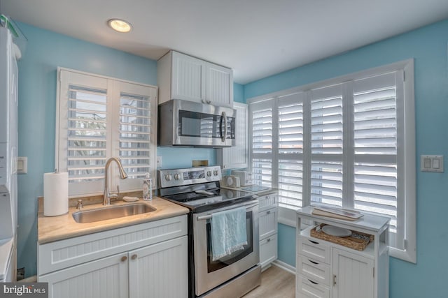 2 E Atlantic St Unit 1, Fenwick Island, DE 19944 - kitchen with appliances with stainless steel finishes, a sink, light countertops, white cabinetry, and light wood-type flooring