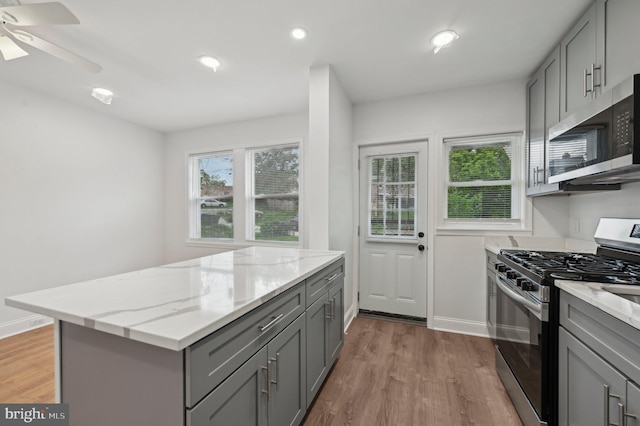 kitchen with gray cabinets, stainless steel appliances, wood finished floors, light stone countertops, and recessed lighting