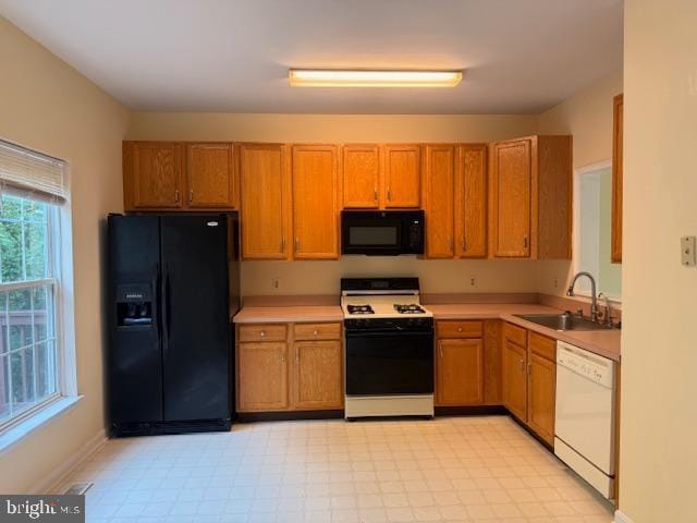 kitchen with a sink, brown cabinets, light floors, black appliances, and light countertops