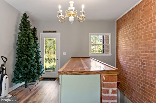 unfurnished dining area with brick wall, a chandelier, and wood finished floors