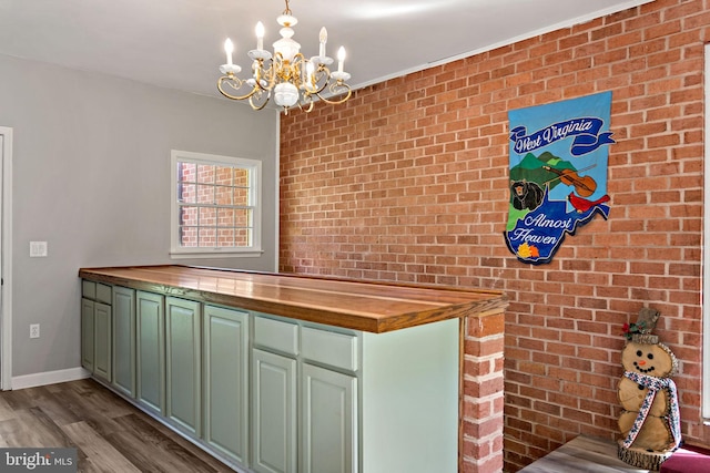 kitchen with wooden counters, brick wall, a chandelier, wood finished floors, and baseboards
