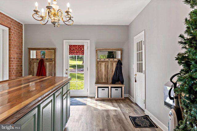 mudroom featuring a chandelier, brick wall, light wood-style floors, and baseboards