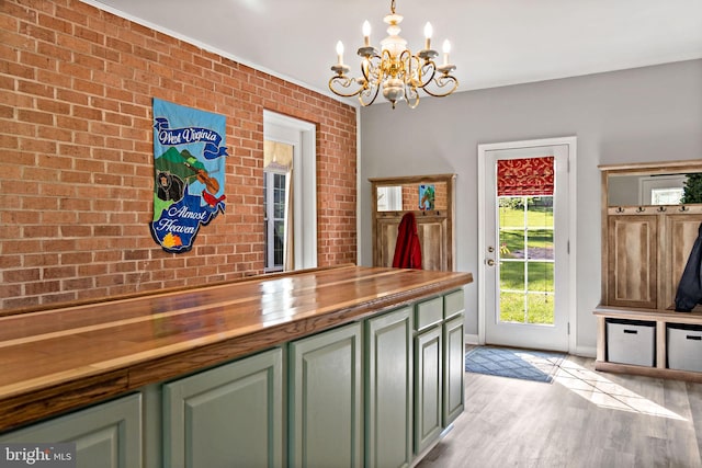 unfurnished dining area with a chandelier, brick wall, baseboards, and light wood-style floors