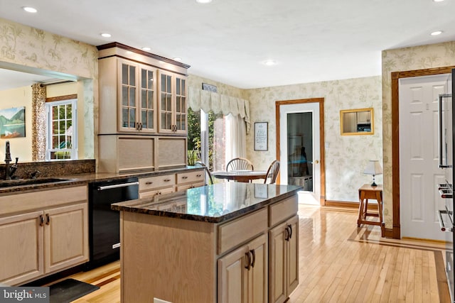 kitchen featuring wallpapered walls, dishwasher, a sink, light wood finished floors, and a kitchen island