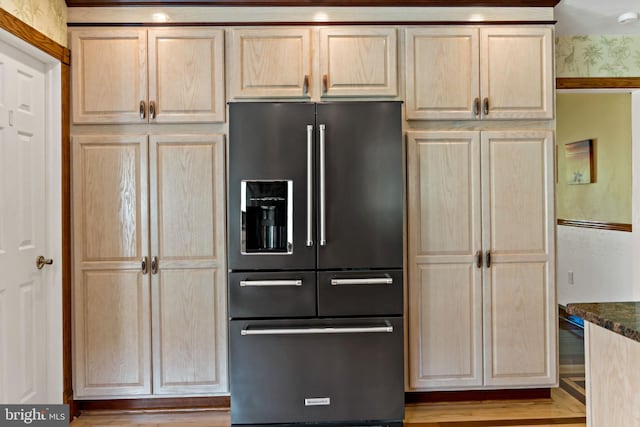 kitchen featuring high end black refrigerator, light brown cabinetry, and dark stone countertops
