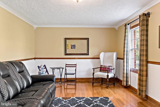living area with wood finished floors, ornamental molding, baseboards, and a textured ceiling