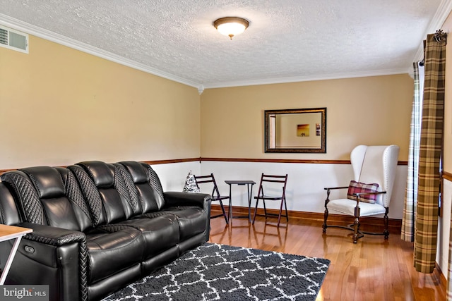 living room featuring a textured ceiling, wood finished floors, ornamental molding, and baseboards