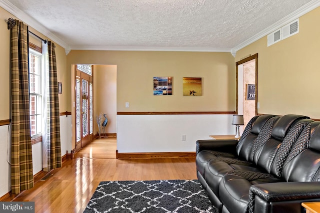 living room with light wood-type flooring, crown molding, a textured ceiling, and baseboards