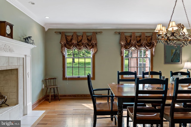 dining room with crown molding, plenty of natural light, light wood-type flooring, a tiled fireplace, and baseboards