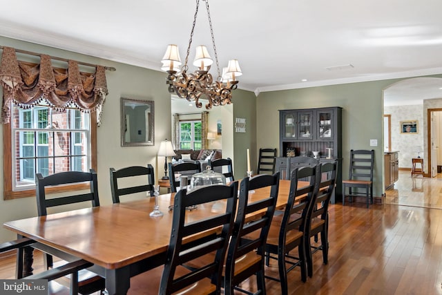 dining room with arched walkways, wood-type flooring, baseboards, a chandelier, and ornamental molding