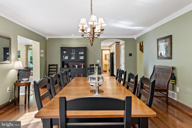 dining room with arched walkways, wood finished floors, a chandelier, crown molding, and baseboards