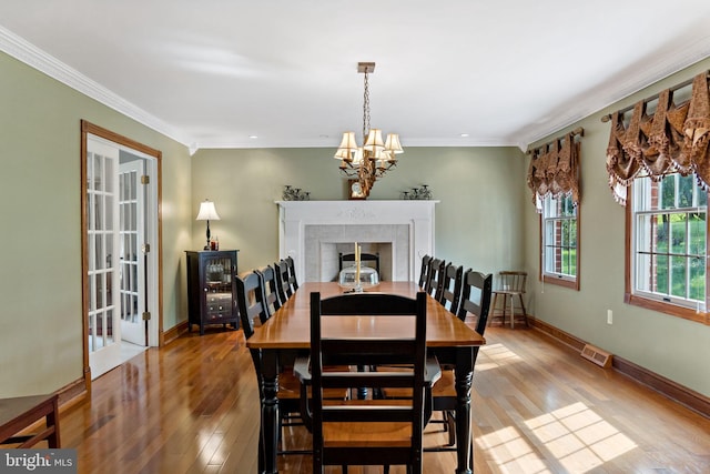 dining room featuring light wood finished floors, ornamental molding, a chandelier, a fireplace, and baseboards
