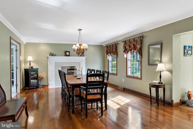 dining area with a chandelier, crown molding, wood finished floors, baseboards, and a tiled fireplace