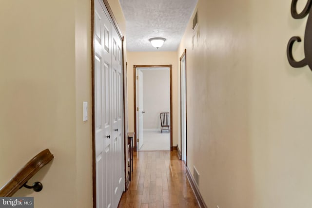 hall featuring a textured ceiling, wood finished floors, and baseboards