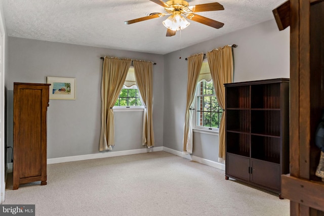 empty room with carpet floors, a textured ceiling, ceiling fan, and baseboards